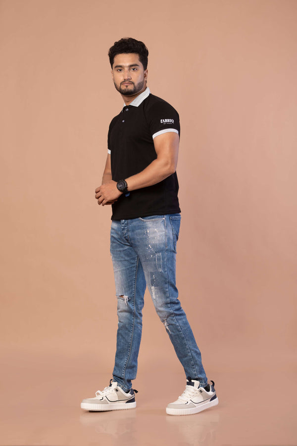 Man wearing a black polo shirt with white accents and blue jeans on a beige background