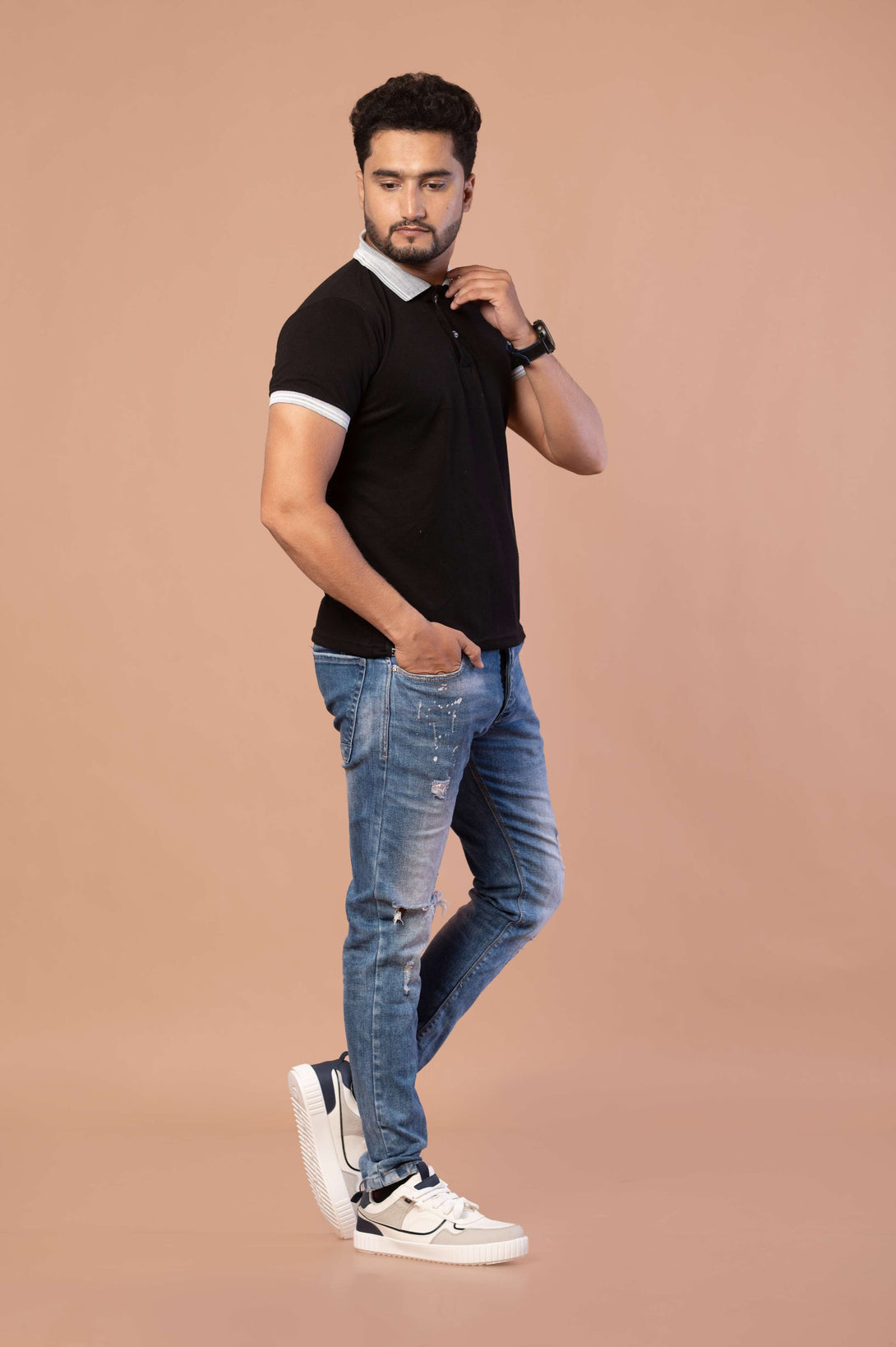 Man wearing a black polo shirt, blue jeans, and white sneakers on a beige background
