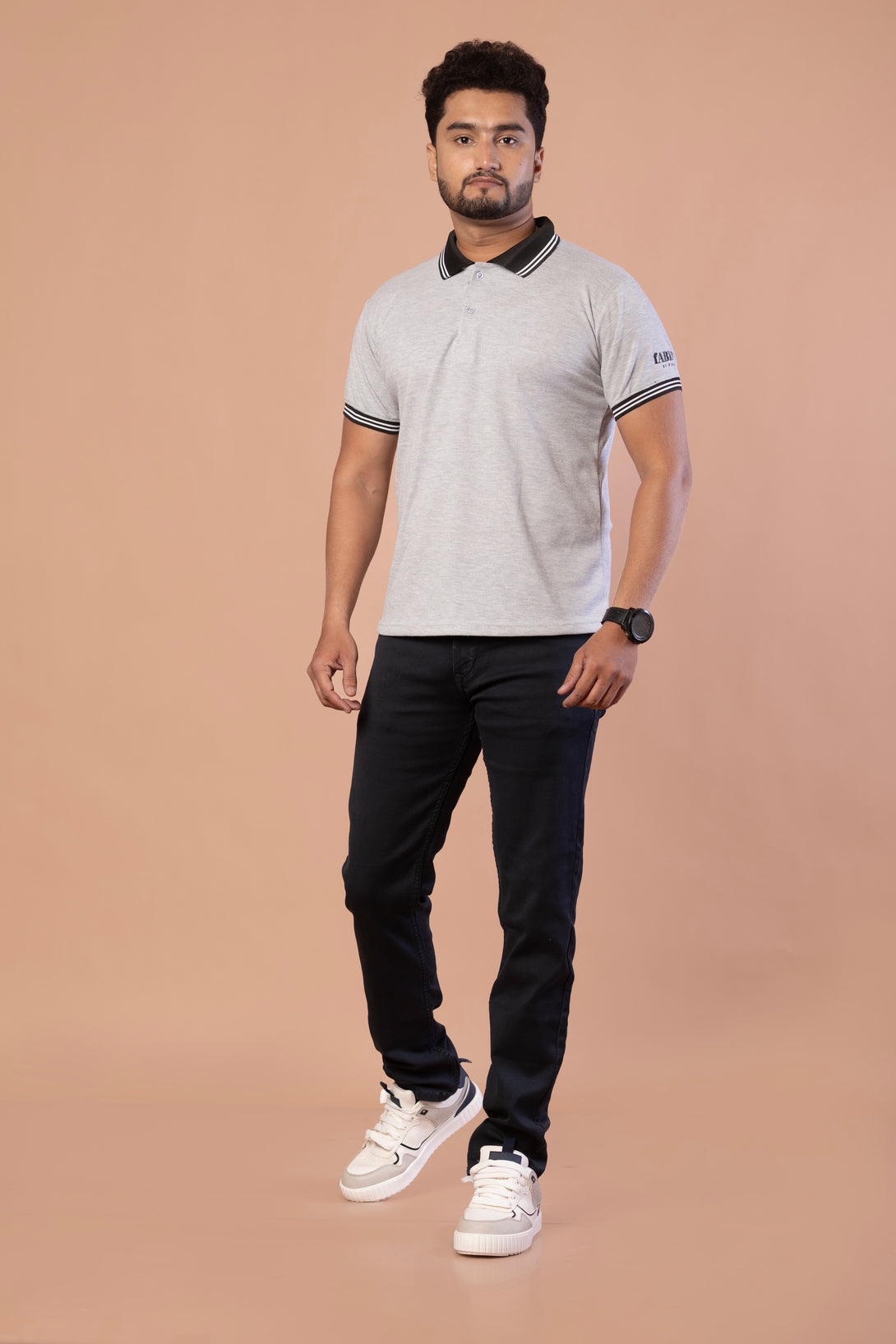 Man wearing a gray polo shirt, black pants, and white sneakers on a beige background