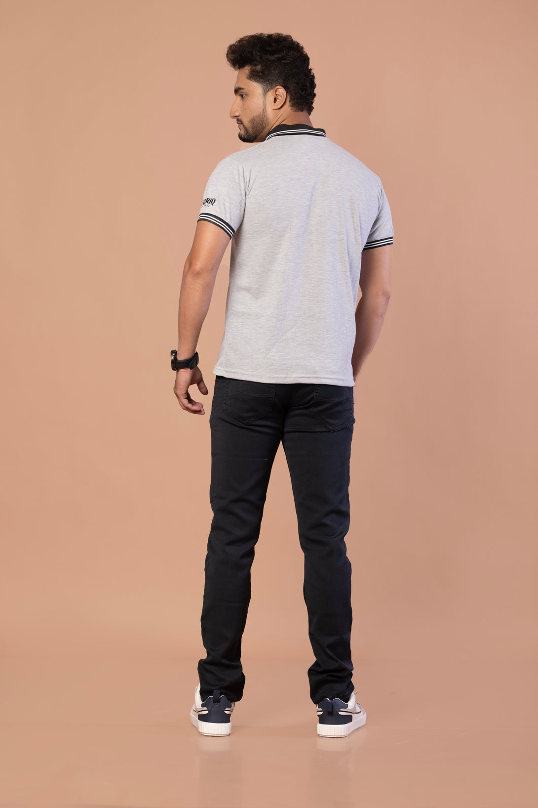 Man wearing a light gray polo shirt and dark jeans on a beige background